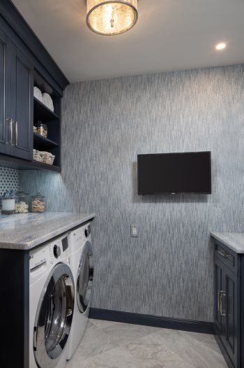 compact laundry room - blue-grey custom cabinetry, blue and white textured wallpaper, lots of storage - showing tv on far wall