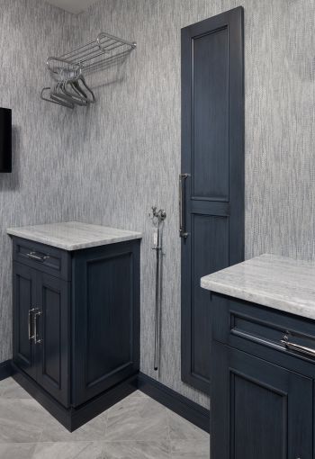 compact laundry room - blue-grey custom cabinetry, blue and white marble countertop, blue and white textured wallpaper, hanging hook, hanging racks, ironing board cupboard
