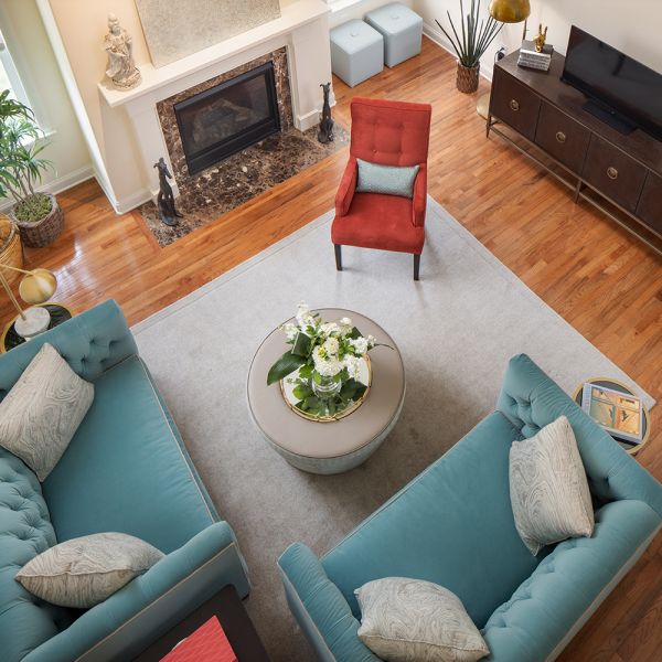 overhead view of living room with light blue loveseat couches, white ottoman and red-orange medium sized armchair, fireplace