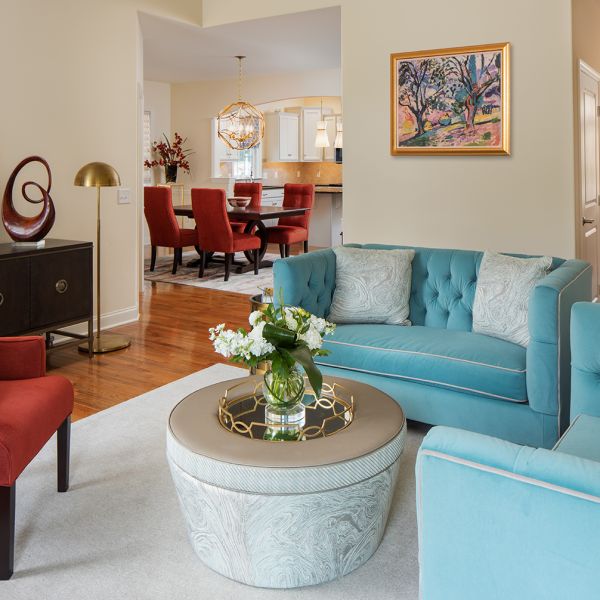 living room with light blue loveseat couches on right, white ottoman, and red-orange medium sized armchair on left, view into dining room