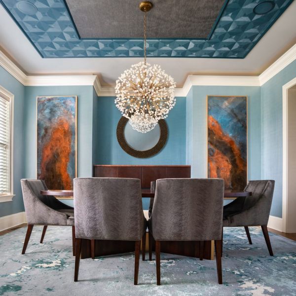 dining room with custom orange and blue artwork on back wall, wallpapered coffered ceiling, blue rug, textured grey dining chairs