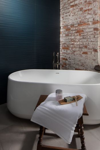 modern industrial master bath - white soaking bath with teal textured wallpaper on left and brick wall on right