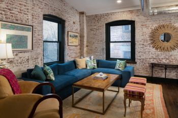 modern furniture and design in industrial warehouse penthouse, rich teal blue couch, yellow armchair, gold mirror, whitewashed brick wall, dark trim