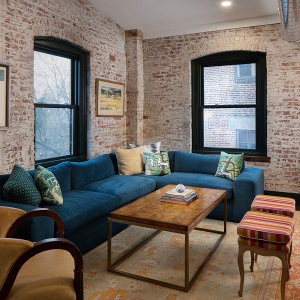 modern furniture and design in industrial warehouse penthouse, rich teal blue couch, yellow armchair, gold mirror, whitewashed brick wall, dark trim