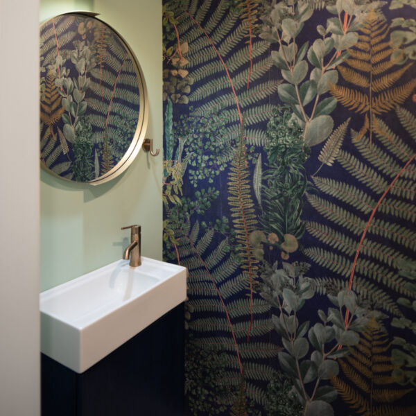 Compact powder room with foliage wallpaper and gold accents.